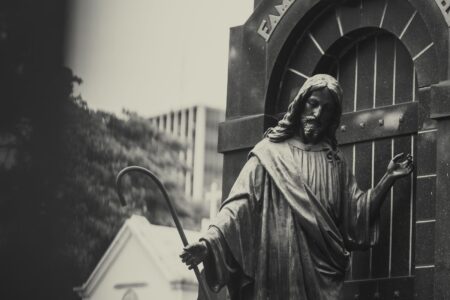 Black and white statue of Jesus Christ holding a cane in a cemetery setting.