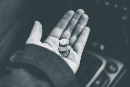 Black and white crop anonymous person demonstrating shiny coins while sitting in car on blurred background